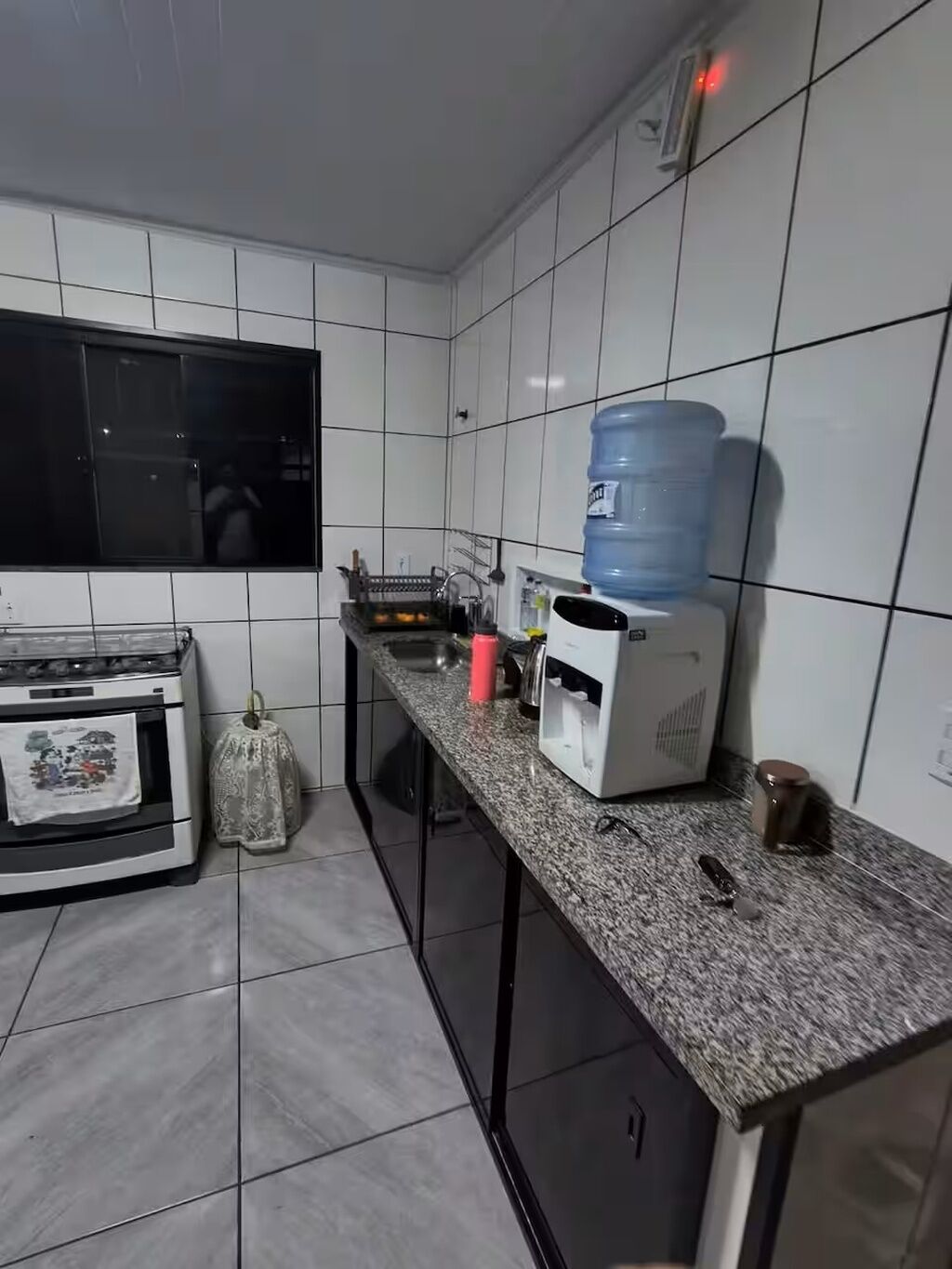 Et køkken med hvide flisevægge, en vanddispenser, kaffemaskine og komfur.