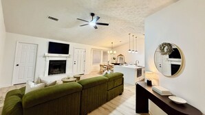 Ein geräumiges Wohnzimmer mit einem grünen Sofa, einem Kamin, einem Fernseher und einer Küchenzeile mit Esstisch.