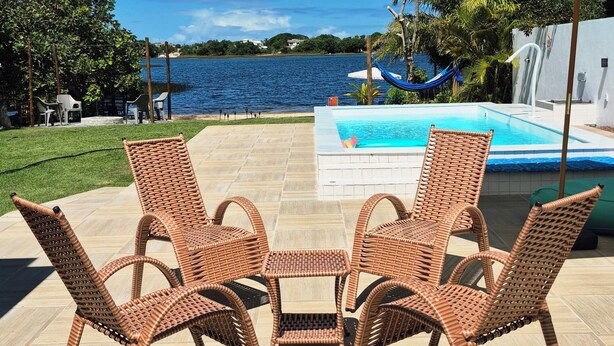 Uma área à beira da piscina com cadeiras e mesa de vime, piscina e vista para a água.