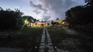 Uma trilha leva a uma casa moderna com caminho de pedra, cercada por vegetação e céu nublado.