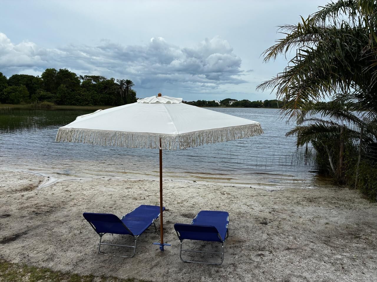 A beach with two blue lounge chairs and a white umbrella.