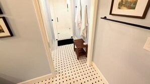 Käytävän lattialla on kuvioitu matto, siellä on myös penkki, pyyhkeet ripustettuina telineeseen ja seinillä on kehystettyjä taideteoksia.