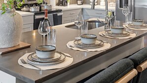 Et moderne køkken med en central ø, stålgrej og et spiseområde med tallerkener, skåle og glas.