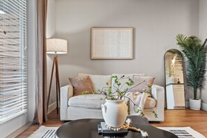 Een woonkamer met een bank, salontafel, lamp, lijst met tekst en een potplant.