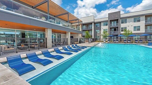 Et moderne hotel med en stor swimmingpool, liggestole og et overdækket udendørs område.
