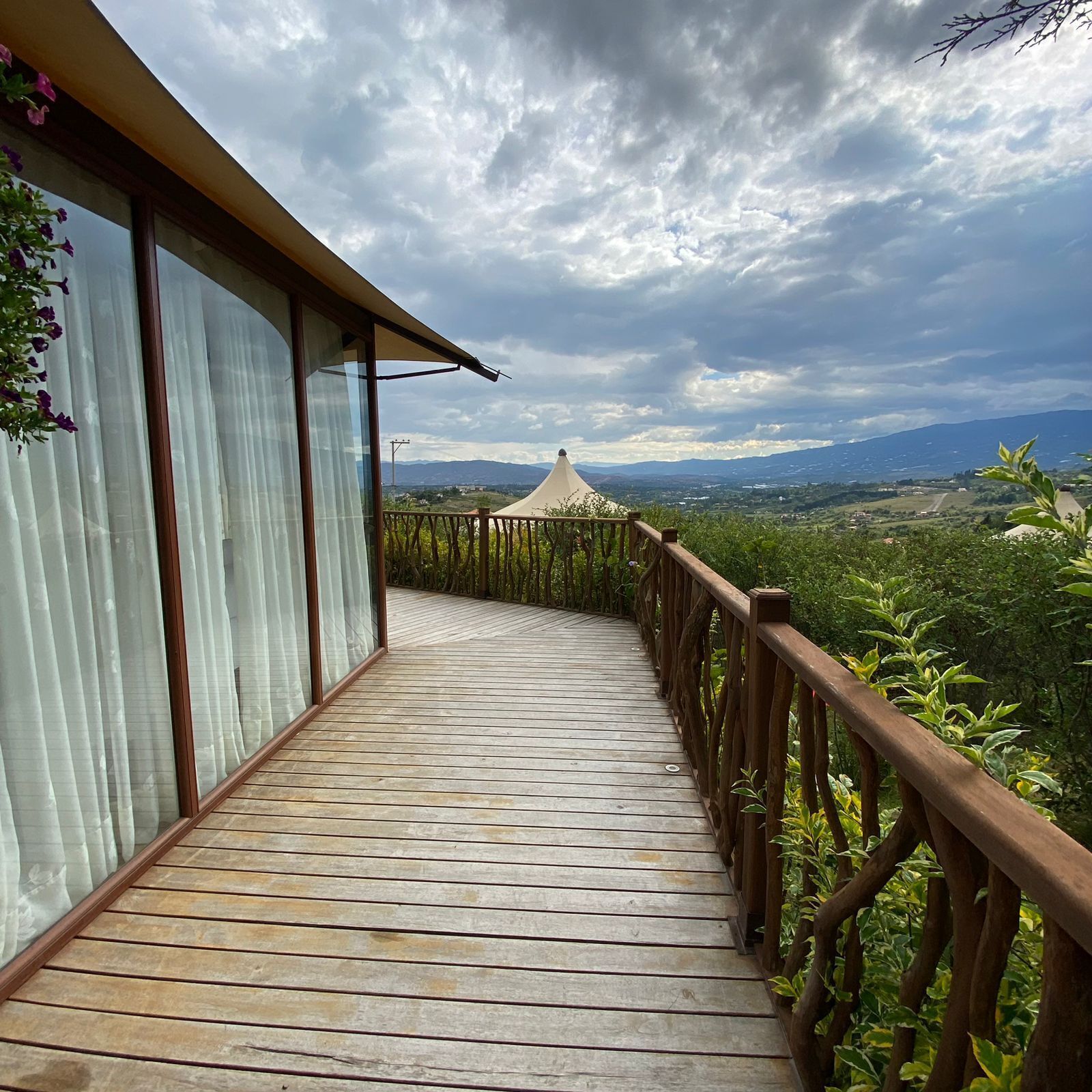 A wooden deck with a railing, leading to a covered area with a view of a mountainous landscape.