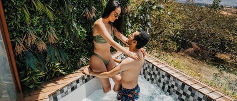 Un jacuzzi con terraza de madera, rodeado de abundante vegetación y vistas al paisaje.