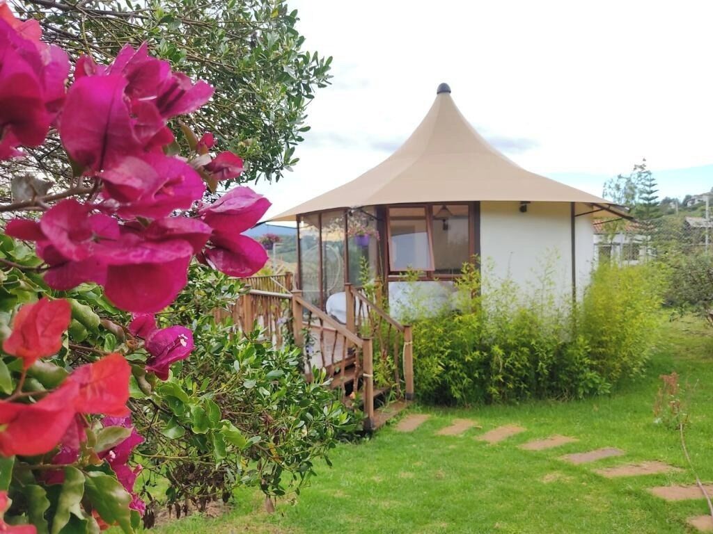 A small, single-story structure with a conical roof, surrounded by a garden with a wooden bench and a pathway.