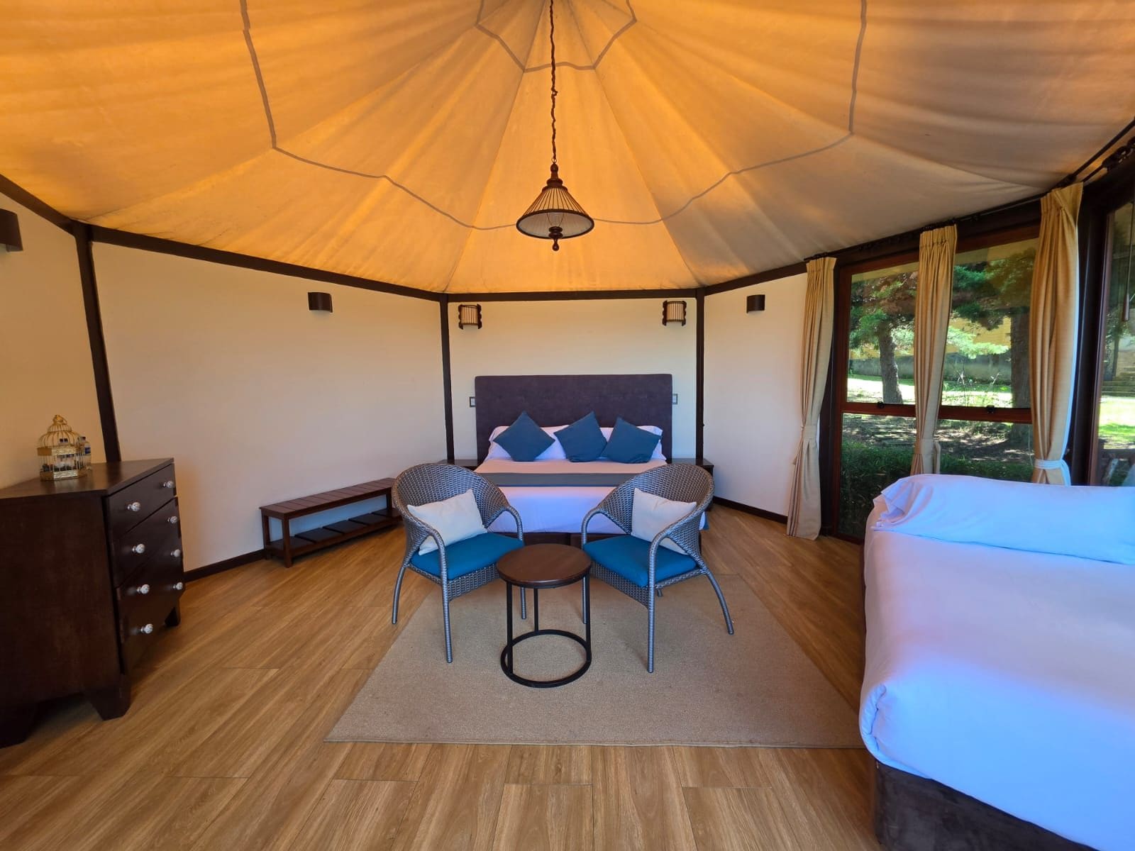 A hotel room with a large bed, two chairs, a small table, a dresser, and a view of the outdoors.
