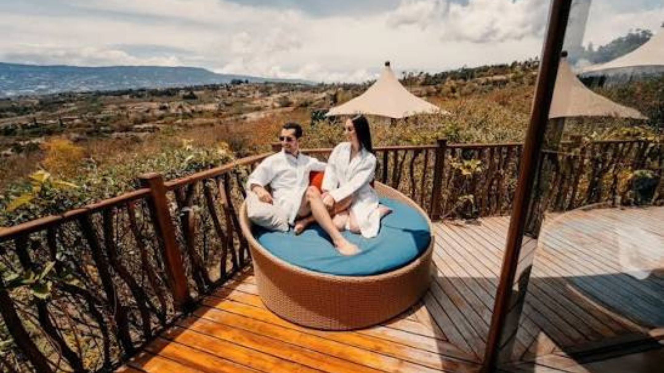 A couple sitting on a round wicker sofa with a view of a landscape.