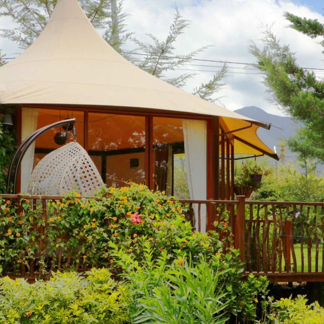 A conical-roofed structure with a wooden deck, surrounded by lush greenery and flowering plants.