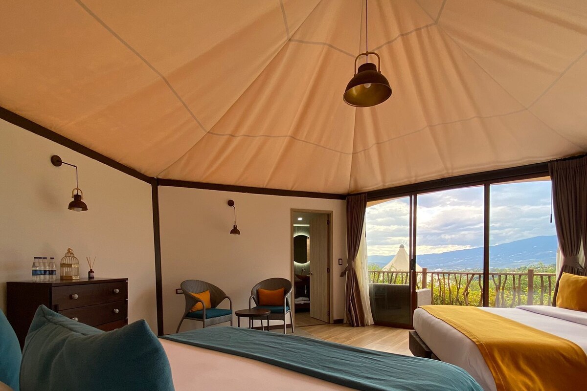 Habitación tipo tienda de campaña con dos camas, una mesita, sillas y vistas del paisaje.