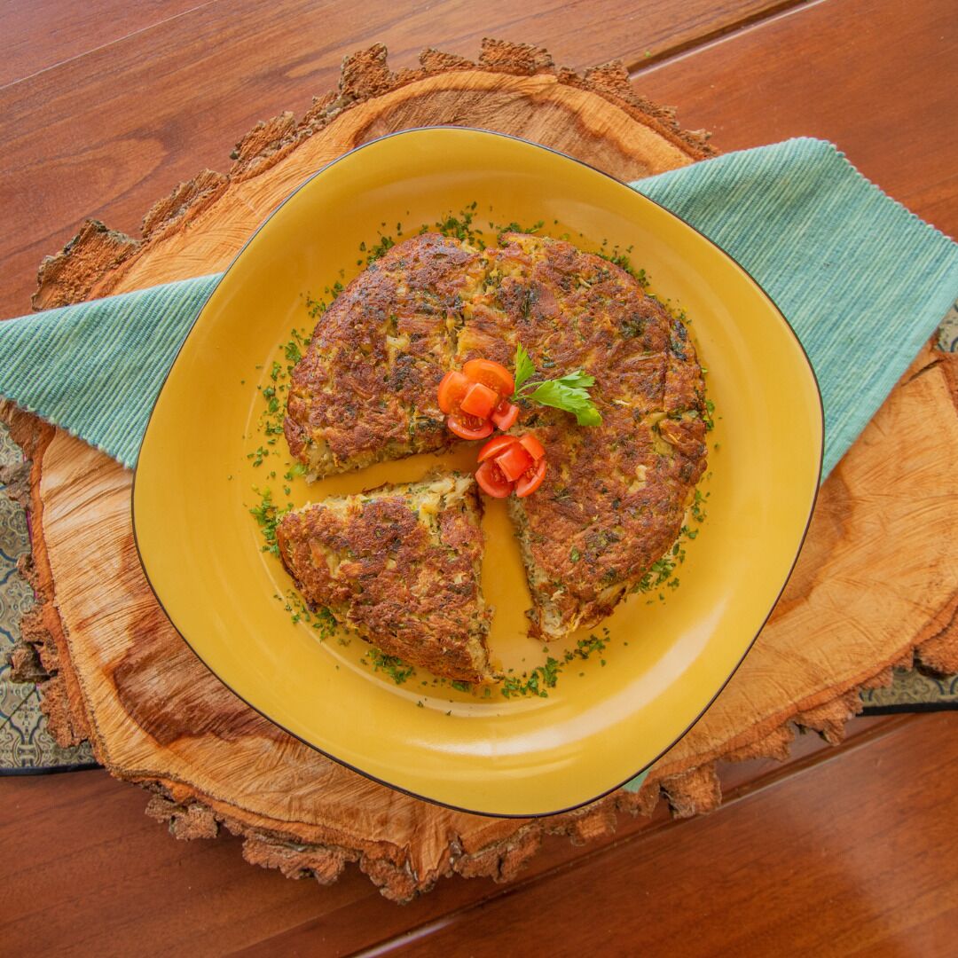 A round, golden-brown dish on a yellow plate, garnished with herbs and tomato slices, placed on a wooden surface.