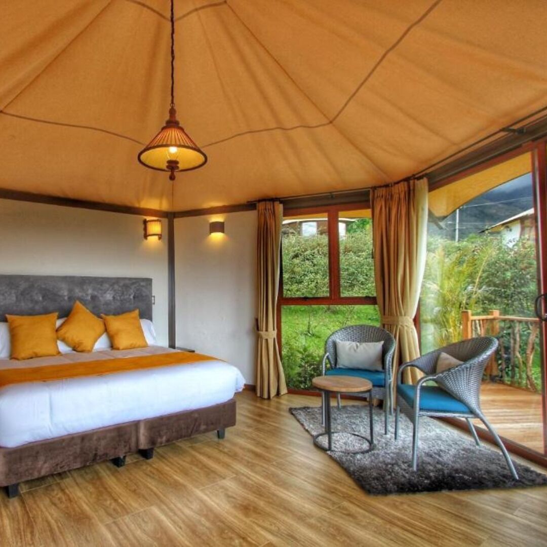 Een slaapkamer met een bed, een stoel, een klein tafeltje en uitzicht op groen buiten.