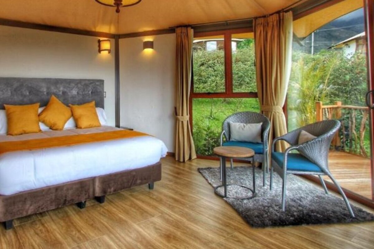 Un dormitorio con cama, una silla, una mesita y vistas al verde exterior.