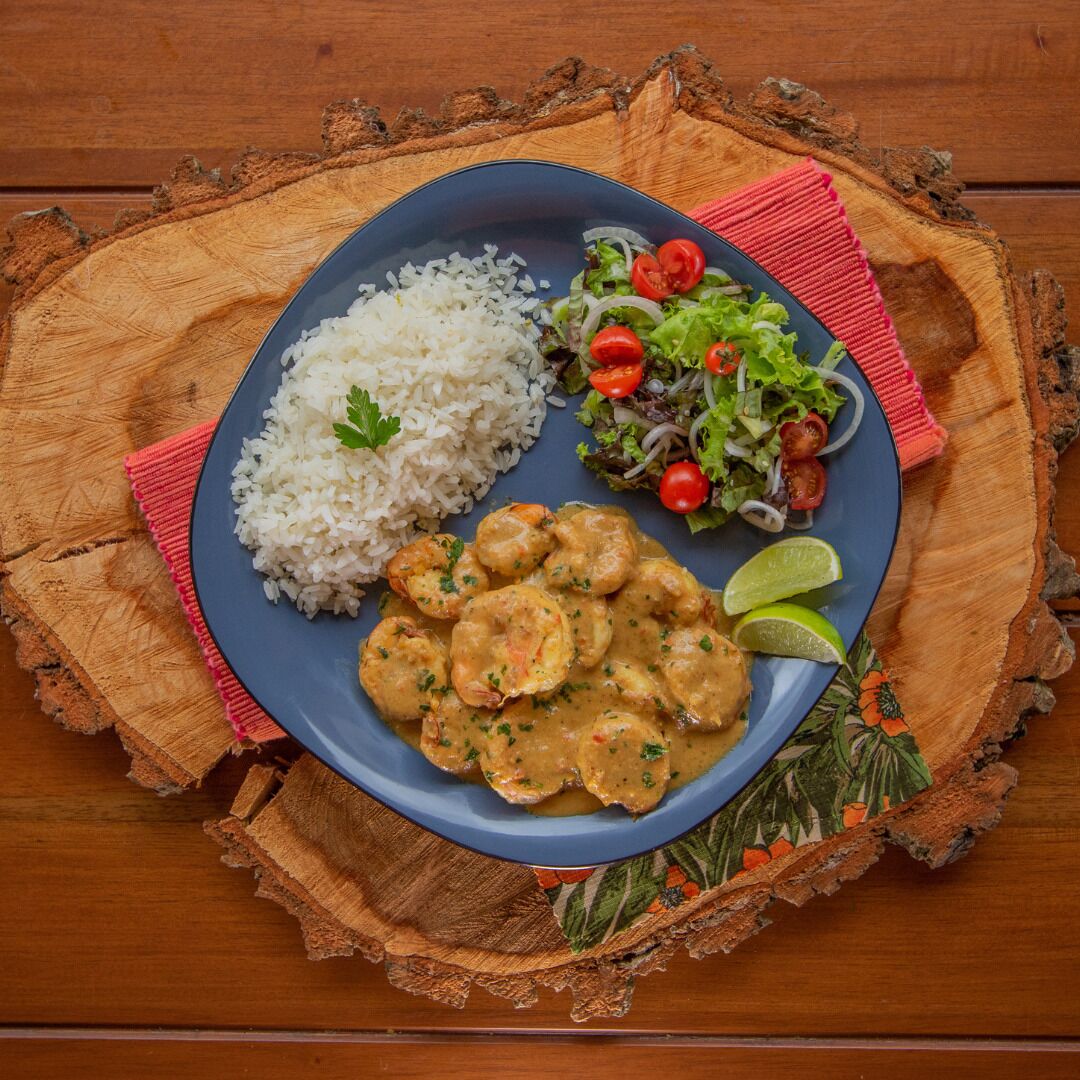 A plate of food with rice, shrimp, and salad on a wooden table.