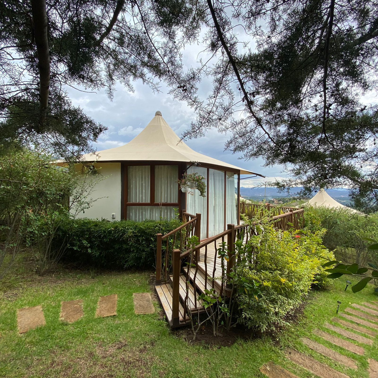 Una cabaña con techo cónico, una escalera de madera y vistas del paisaje circundante.