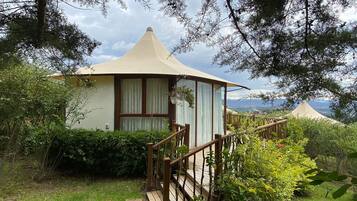 Una cabaña con techo cónico, una escalera de madera y vistas del paisaje circundante.