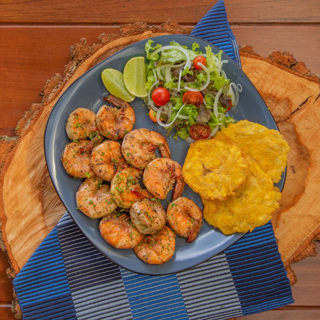 Een bord met garnalen, salade en gebakken plantain.