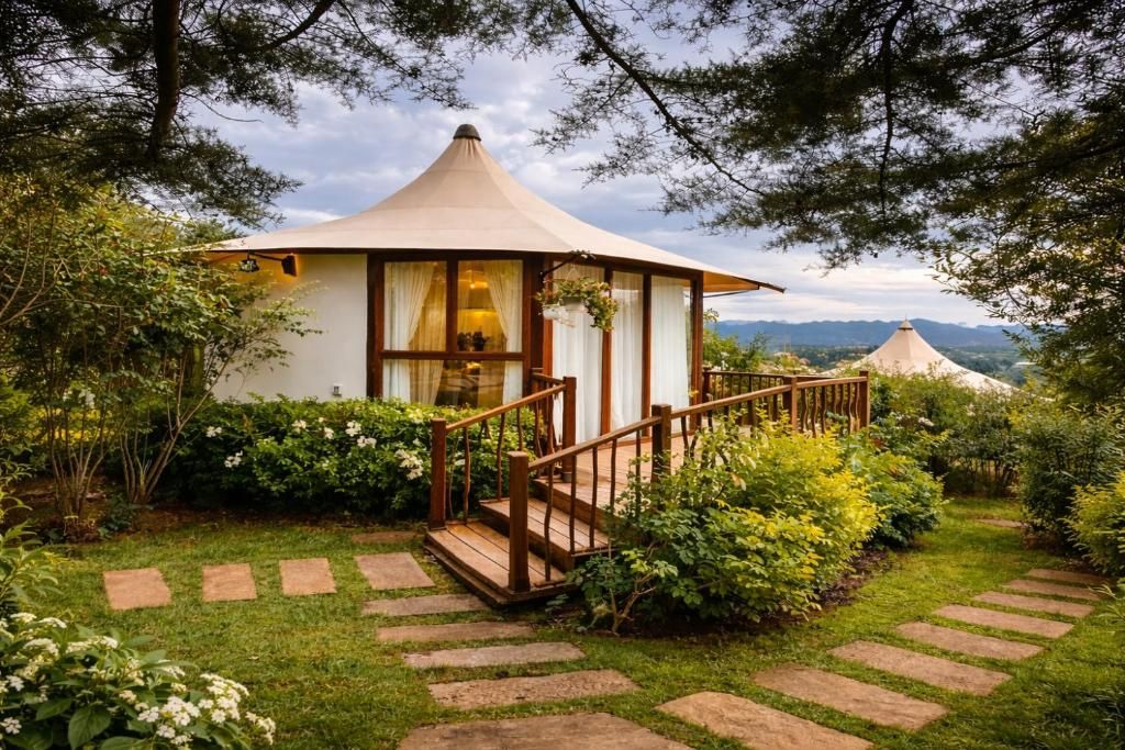 Uma estrutura em estilo de gazebo com escadaria de madeira que a leva, cercada por vegetação exuberante e um caminho de pedra.