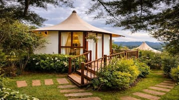 Uma estrutura em estilo de gazebo com escadaria de madeira que a leva, cercada por vegetação exuberante e um caminho de pedra.