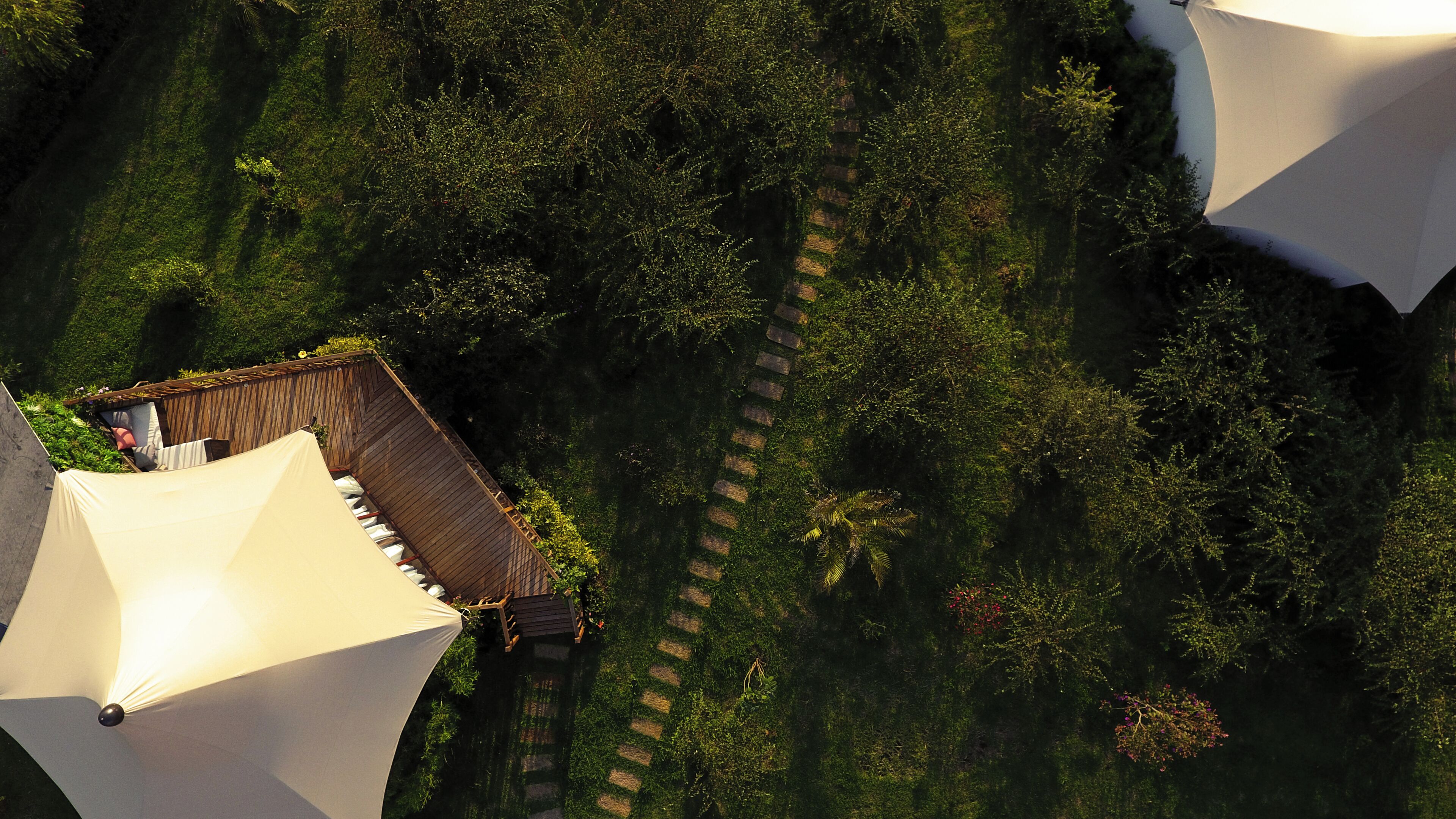 An aerial view of a resort with a wooden deck, a white tent, and lush greenery.