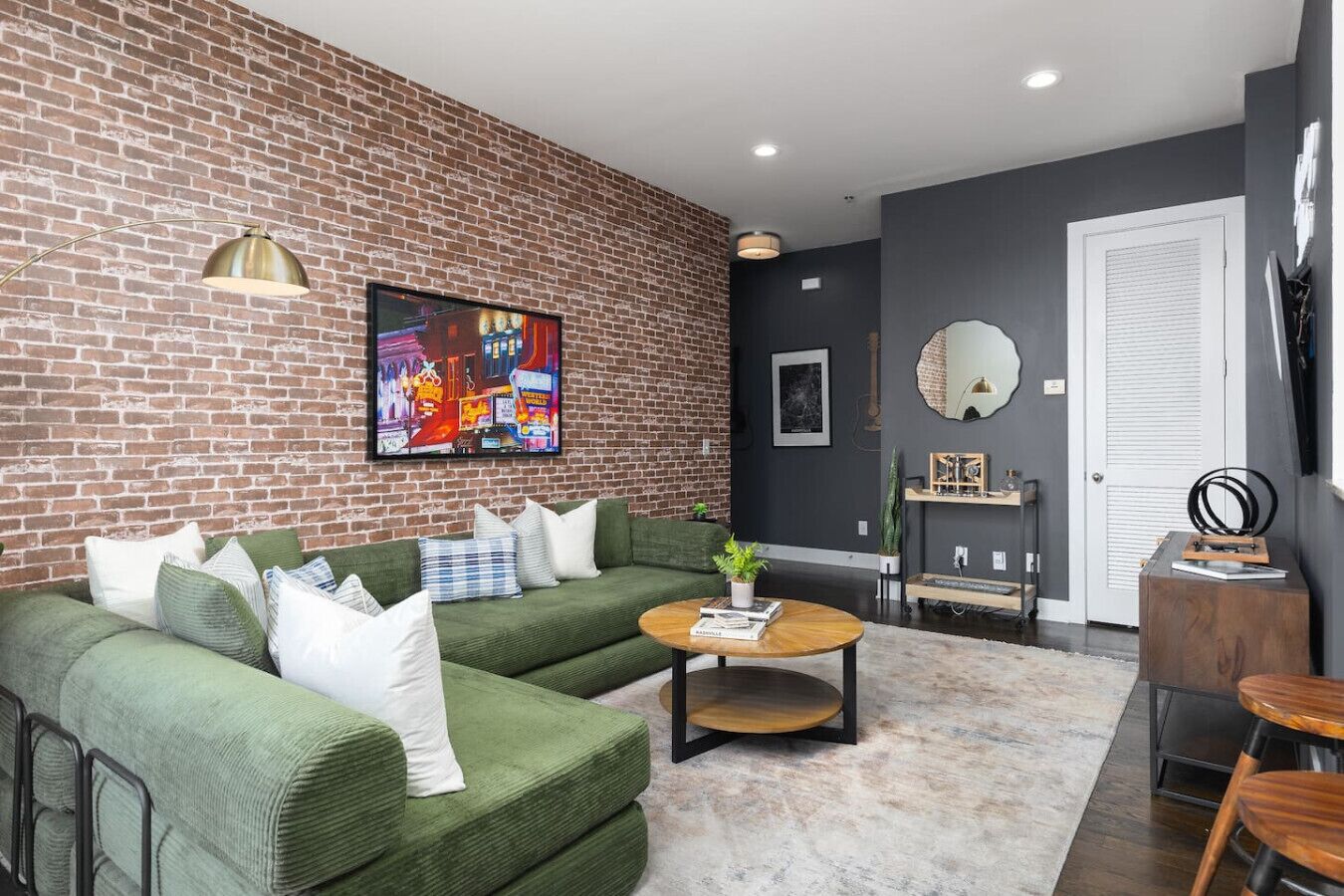 A living room with a brick wall, green sofa, coffee table, and a TV mounted on the wall.