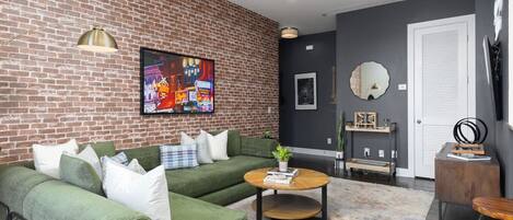 A living room with a brick wall, green sofa, coffee table, and a TV mounted on the wall.