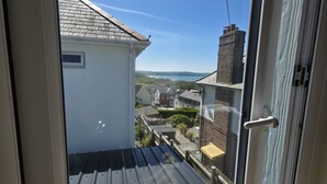 En vy från ett fönster med ett tak av metall och en vit vägg, med utsikt över ett bostadsområde med hus och en klar himmel.