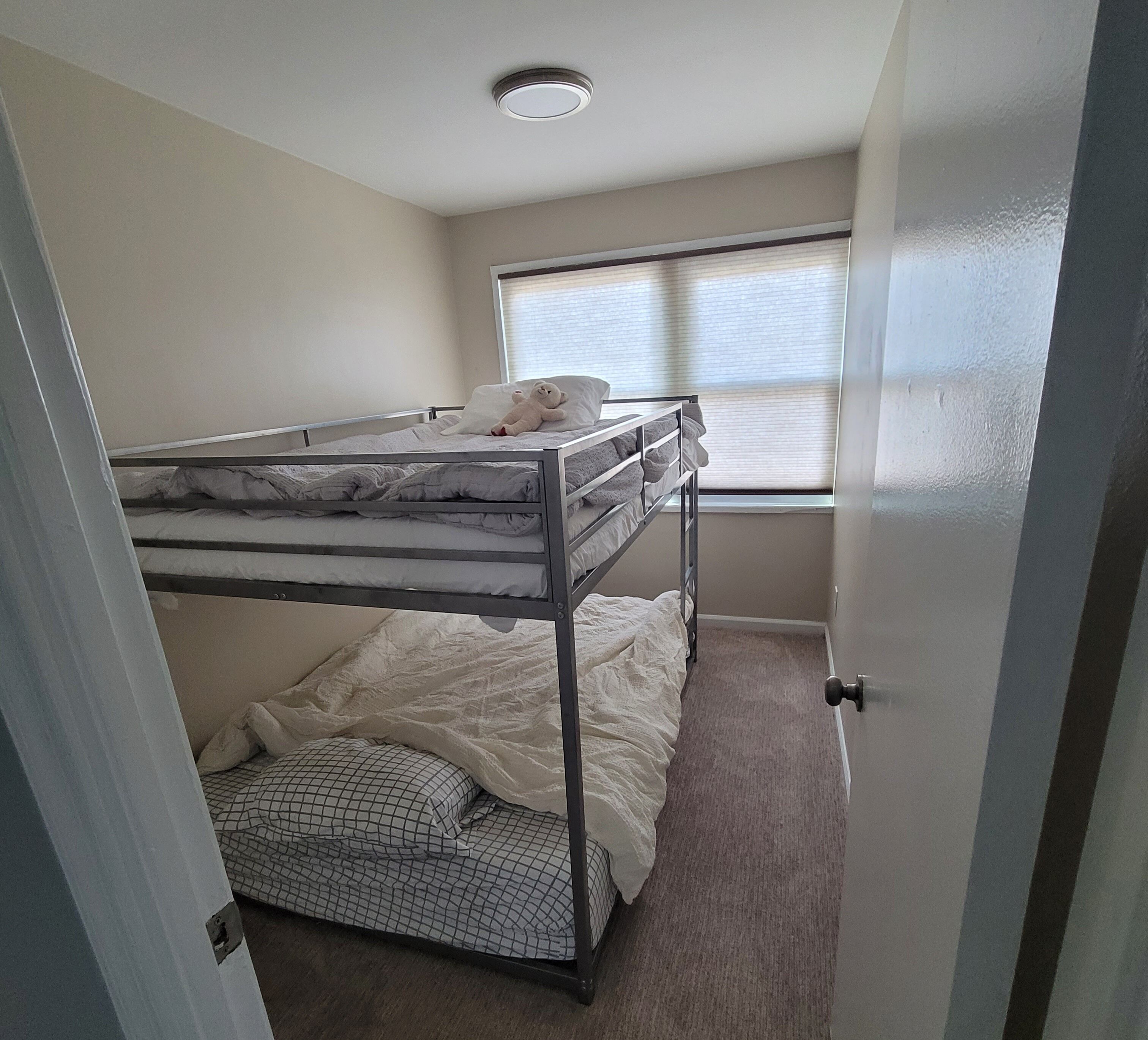 A bunk bed room with a window, carpeted floor, and a door.