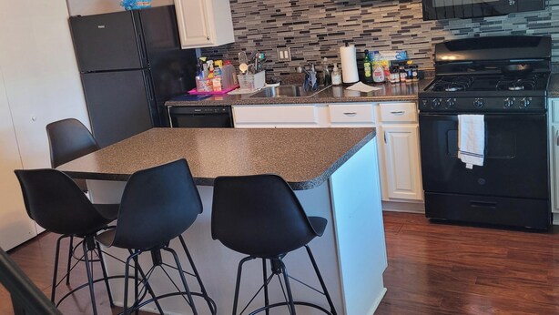 A kitchen with a granite countertop, white cabinets, a black refrigerator, a microwave, a stove, and a bar stool area. - Gorgeous 3-bedroom townhome with AC in friendly Dundalk (Dundalk)