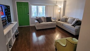 A living room with a green door, two couches, a yellow armchair, a TV, and a window with blinds. - Gorgeous 3-bedroom townhome with AC in friendly Dundalk (Dundalk)