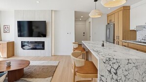 Una cucina moderna con piani di lavoro in marmo, pensili in legno e illuminazione a sospensione.