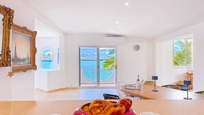 Ett rum med ett matbord, två vita koppar, en röd skål med mat och ett stort fönster med utsikt över havet.