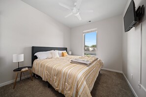 Une chambre à coucher comprenant un lit, une table de chevet, une lampe, un ventilateur de plafond, un téléviseur et une fenêtre donnant sur un beau paysage.