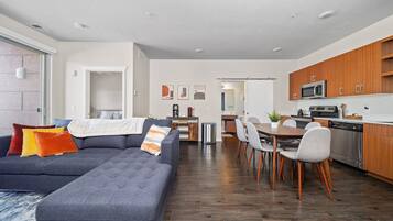 Een moderne woonkamer met een modulaire bank, een eethoek, een keuken en een zichtbare deur naar een andere kamer.