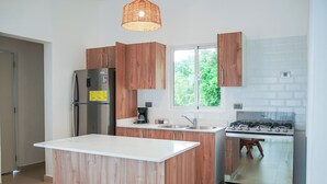 Une cuisine moderne avec des meubles en bois, un îlot central intégré, des appareils électroménagers en acier inoxydable et une fenêtre donnant sur un paysage verdoyant.