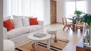 Un salon moderne avec un canapé blanc, une table basse ronde et un coin repas avec des chaises en bois.