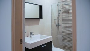 Une salle de bain avec un lavabo blanc, un meuble noir et une cabine de douche en verre.