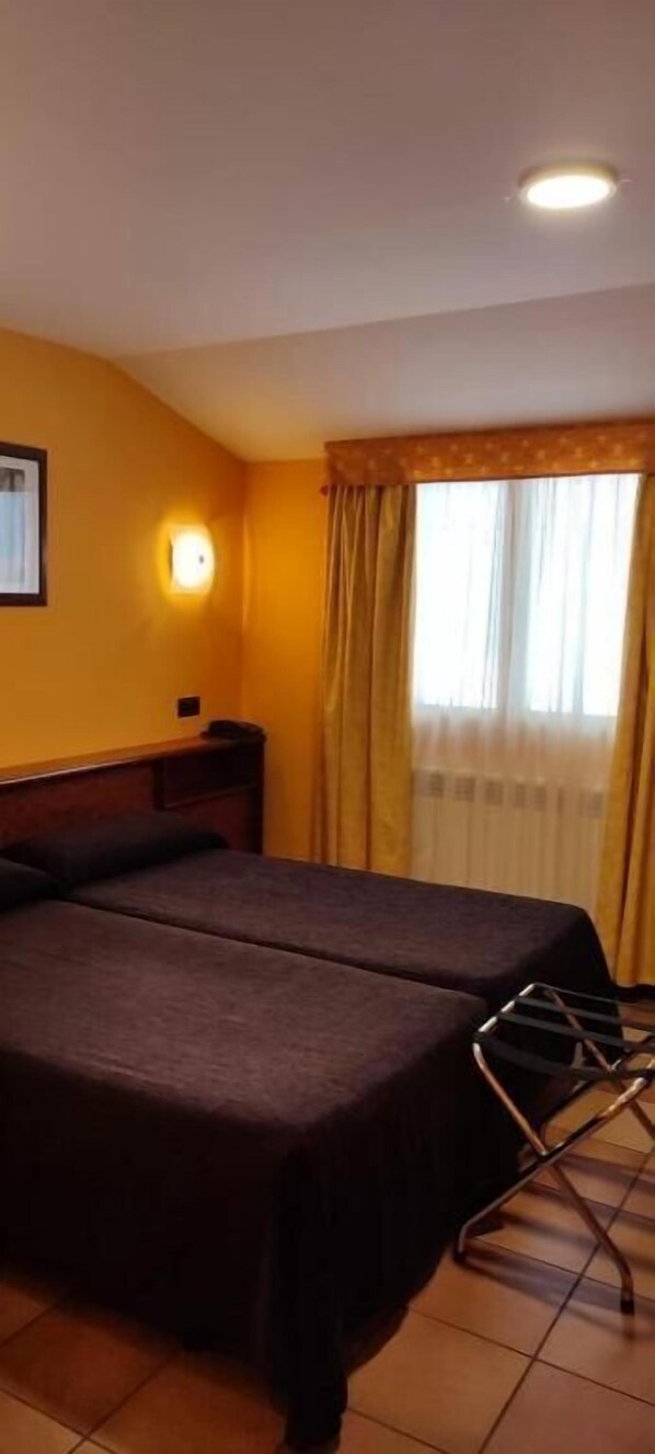 A hotel room with two beds, a nightstand, a lamp, and a window with curtains. - Aparthotel Ransol (Ransol)