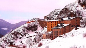 A historic building with a stone facade, located on a snow-covered hillside with a mountainous backdrop. - Aparthotel Ransol (Ransol)