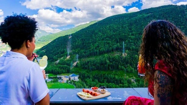 A person with a drink, another with a plate of food, and a scenic view of a valley with mountains and power lines. - Aparthotel Ransol (Ransol)