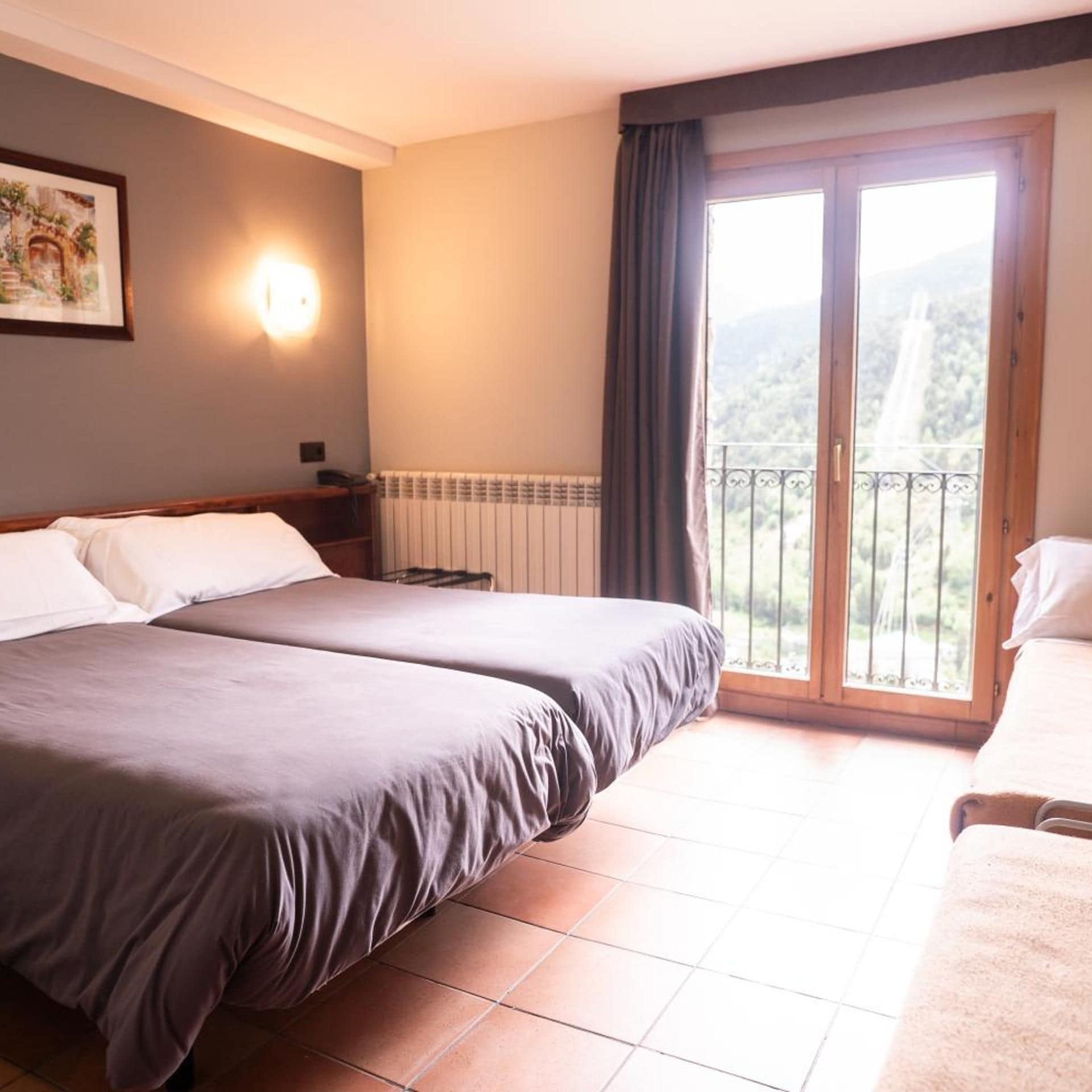 A hotel room with two beds, a radiator, a nightstand, a wall-mounted lamp, and a balcony with a view.