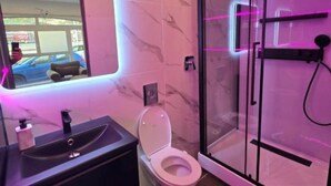 A bathroom with a marble wall, a sink, a toilet, and a glass shower enclosure. - LoVe 3 au Falaises (Agde)