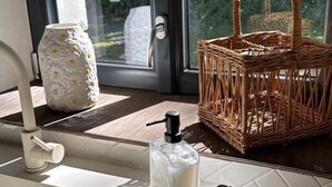 Ein Badezimmer mit Fenster, einem Korbwäschesessel, einer Milchflasche, einem Schwamm und einem Handtuch.