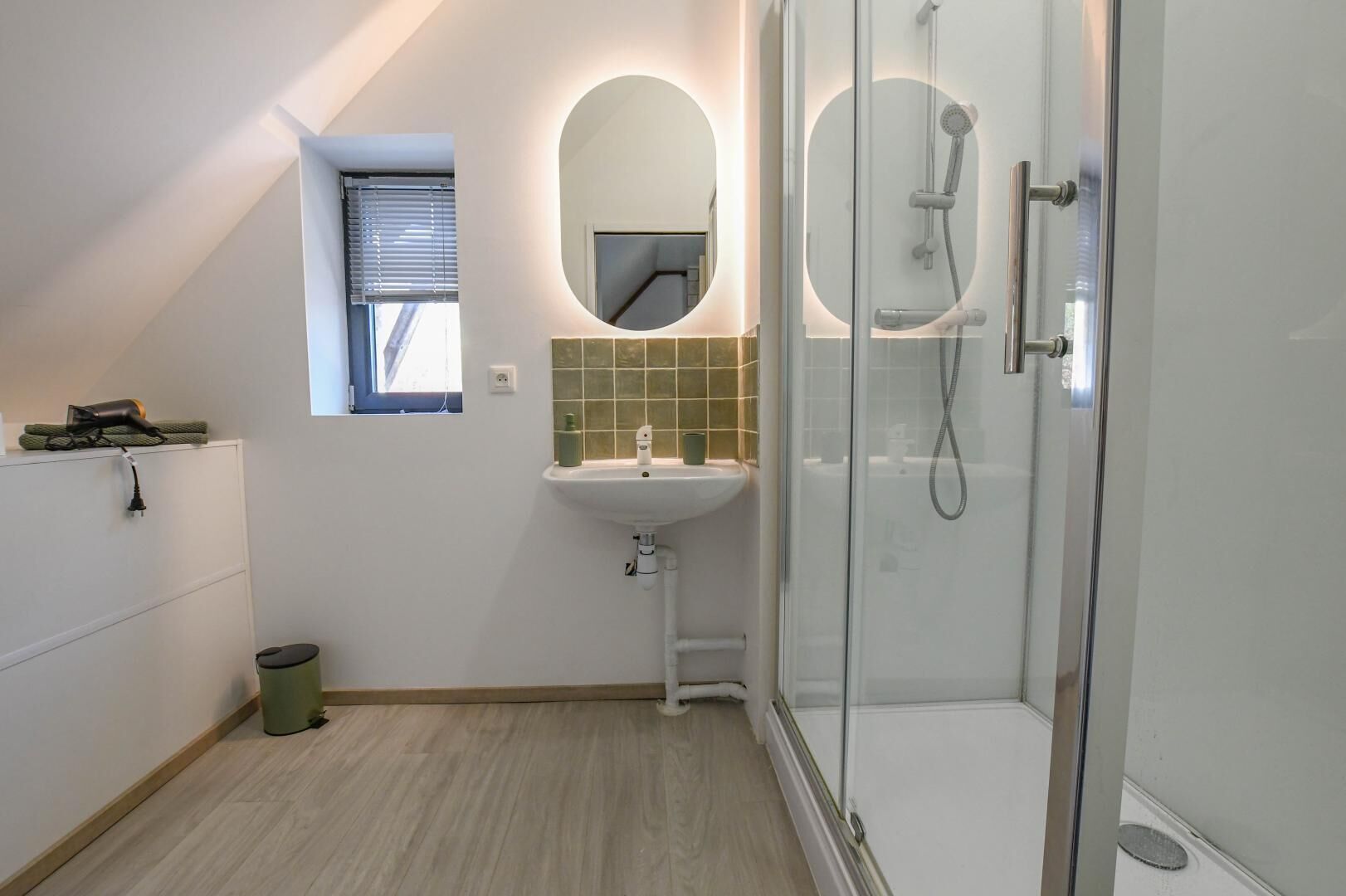 A modern bathroom with a shower, sink, and a small window.