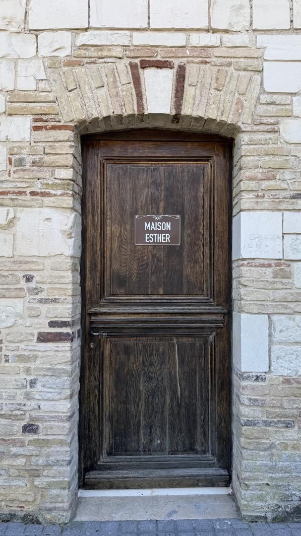 Un mur de pierre avec une porte en bois portant l’inscription « MAISON ESTHER ».