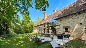 Ein Steinhaus mit Terrasse, Außenbestuhlung und einem gläsernen Anbau.