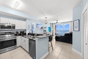 A modern kitchen with stainless steel appliances, a dining area with a view, and a cozy living space with a sofa. - 24th Floor Beach Front Condo! Amazing Views! (Panama City)