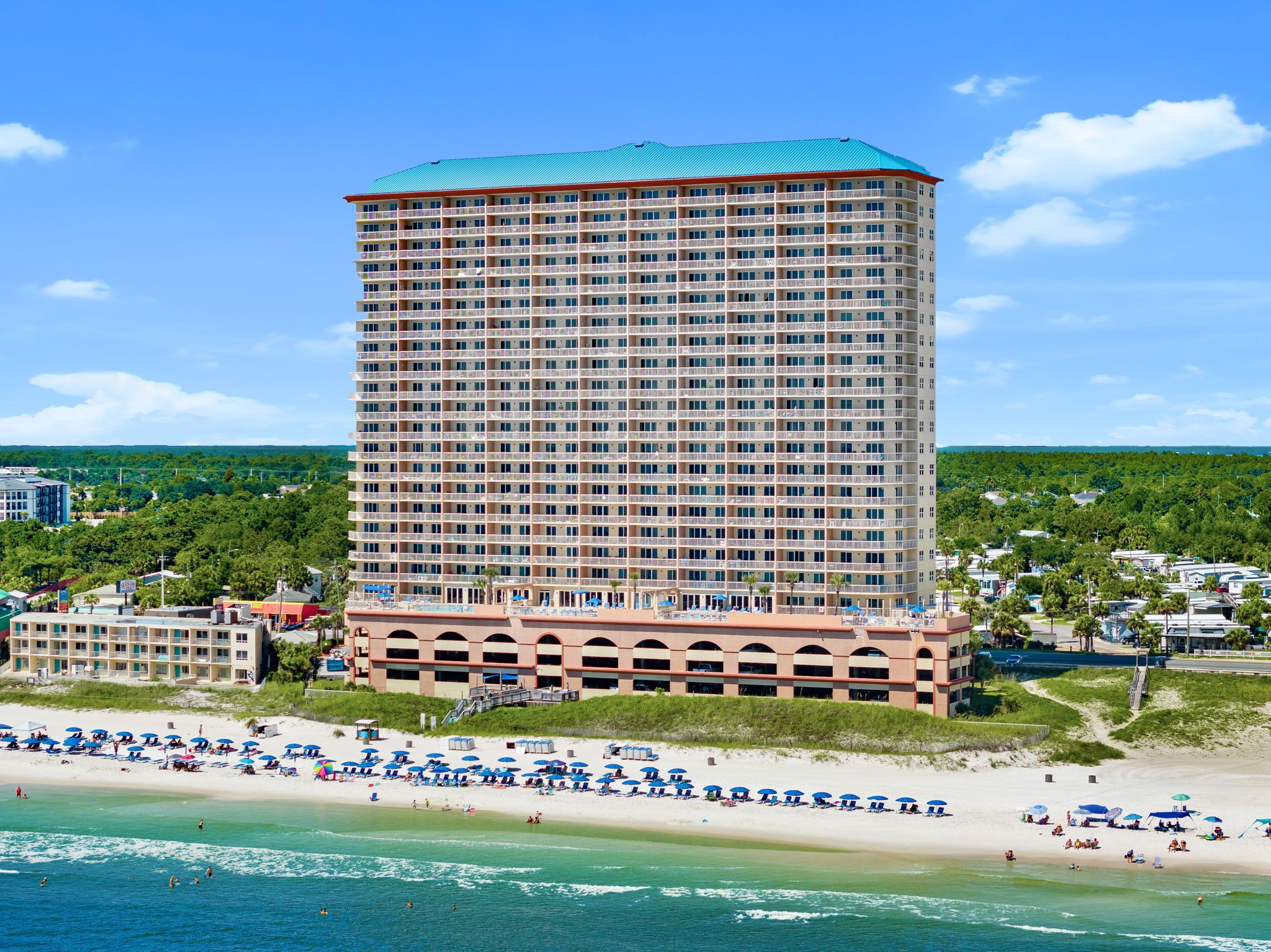 Ein mehrstöckiges Hotel in Strandlage mit Balkonen, einem Poolbereich und Blick auf den Ozean.